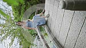 Beautiful young hispanic woman wearing glasses smiling sitting on a bridge at japanese park