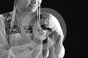 Beautiful young hispanic woman wearing light colored blouse with traditional embroided edges, braiding her own hair