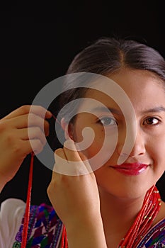 Beautiful young hispanic woman wearing white blouse with traditional embroided edges, attaching red hair extensions