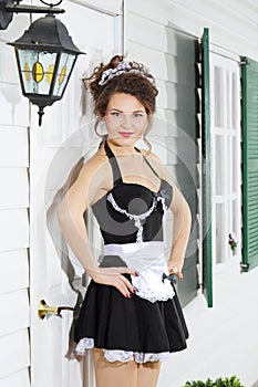 Beautiful young housemaid stands near front door of house