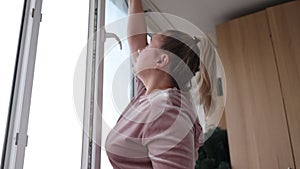 Beautiful young housewife in working clothes washing windows by professional tools at home.