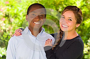 Beautiful young interracial couple in garden environment, embracing and smiling happily to camera