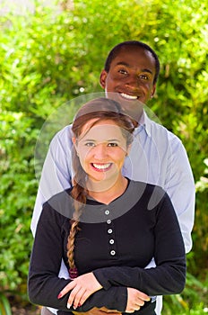 Beautiful young interracial couple in garden environment, embracing and smiling happily to camera