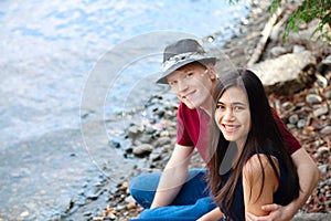 Beautiful young interracial couple sitting together by lake shore