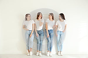 Beautiful young ladies in jeans and white t-shirts near wall indoors. Woman`s Day
