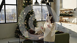 A beautiful young lady adjusting a virtual reality headset near a Christmas tree.
