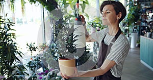 Beautiful young lady florist sprinkling green potted plant in flower shop