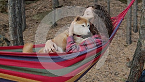 Beautiful young lady hugging cute shiba inu doggy swinging in hammock relaxing in forest on autumn day