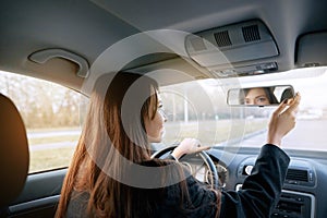 Beautiful young lady looking back through the rear view mirror of a car while reversing.