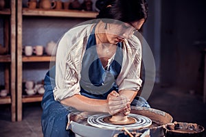 Beautiful young lady making ceramic pottery on wheel. Pottery workshop.