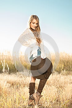 Beautiful young lady model posing in a field at sunrise with a hat in hand