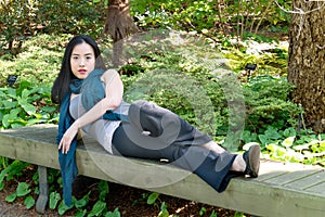 Beautiful young lady reclines on an outdoor park bench