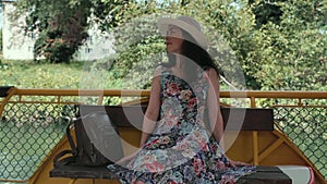 A beautiful young lady in a straw hat and dress is sitting and admiring nature. The concept of summer vacations and