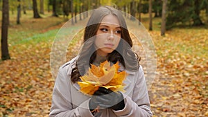 Beautiful young lady waiting for someone in the autumn park plaing with mapleleaf bouquet smile to someone