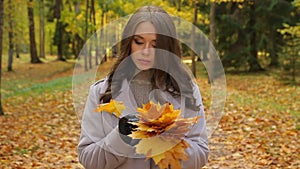 Beautiful young lady worrying, plaing with mapleleaf bouquet, smile to someone