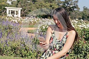 Beautiful young Latin woman in a park receiving text messages on her cell phone. Technology and communication concept