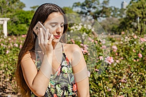 Beautiful young Latin woman in a park talking on her cell phone. Technology and communication concept