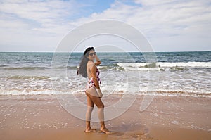 Beautiful and young latin woman is walking along the shore of the beach and posing for photos. Beautiful woman is on holiday on a