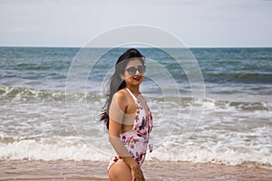 Beautiful and young latin woman is walking along the shore of the beach and posing for photos. Beautiful woman is on holiday on a
