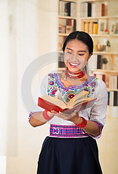 Beautiful young lawyer wearing black skirt, traditional andean blouse with necklace, standing posing for camera, holding