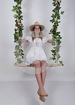 Beautiful young leggy blonde in a little white dress and white cowboy hat on a swing, wooden swing suspended from a rope