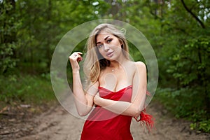 Beautiful young long-haired blonde in a red dress posing on the road in a summer park with a ripe strawberry fruit in her hand.