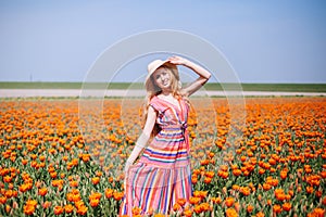 Beautiful young long red hair woman wearing in striped dress and straw hat standing on colorful flower tulip field in Holland