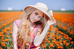 Beautiful young long red hair woman wearing in striped dress and straw hat standing on colorful flower tulip field in Holland