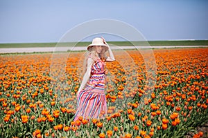 Beautiful young long red hair woman wearing in striped dress and straw hat standing on colorful flower tulip field in Holland