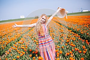 Beautiful young long red hair woman wearing in striped dress and straw hat standing on colorful flower tulip field in Holland