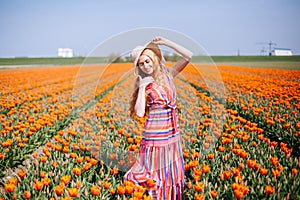 Beautiful young long red hair woman wearing in striped dress and straw hat standing on colorful flower tulip field in Holland