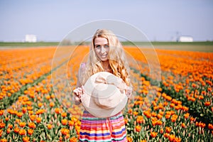 Beautiful young long red hair woman wearing in striped dress and straw hat standing on colorful flower tulip field in Holland