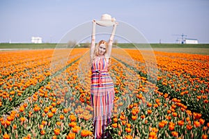 Beautiful young long red hair woman wearing in striped dress and straw hat standing on colorful flower tulip field in Holland