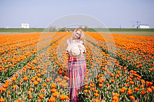 Beautiful young long red hair woman wearing in striped dress and straw hat standing on colorful flower tulip field in Holland