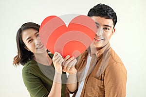 Beautiful young loving couple is holding a card in the shape of heart over white background