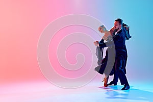 Beautiful young man and handsome woman, ballroom dancers making performance, dancing against gradient pink blue