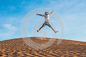 Beautiful young man jumping barefoot on sand in desert enjoying nature and the sun. Fun, joy and freedom