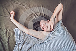 Beautiful young man lying down in bed and sleeping, top view. Do not get enough sleep concept