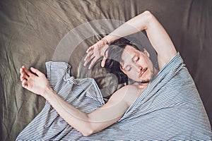 Beautiful young man lying down in bed and sleeping, top view. Do not get enough sleep concept