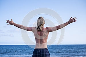 Beautiful young man viewed from rear with open arms in front of the ocean and freedom. success and enjoyment concept for young