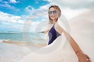 Beautiful young mature woman smiles joyfully in sunglasses in a swimsuit with a white scarf on a tropical paradise beach