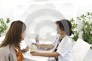 Beautiful young mixed race female doctor with pregnant patient in front of attendee, pill jar holder