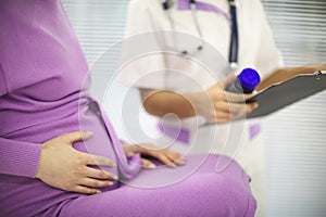 Beautiful young mixed race female doctor with pregnant patient in front of attendee, pill jar holder