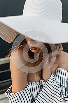 Beautiful young model girl in a white fashionable hat on the beach. Woman in summer fashion clothes on weekend