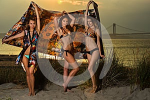 Beautiful young models wearing bikinis posing at sunset beach.