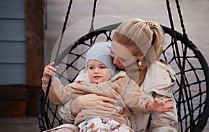 Beautiful Young Mom and baby hugging and have fun. Mother holding her son. Models wearing knitted beige sweater, jacket, beanie