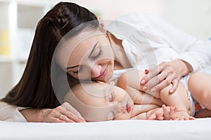 Beautiful young mom looking at her sleeping little baby and smiling. Child lying in bed at home