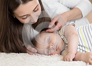 Beautiful young mom looks at baby sleeping in bed at home