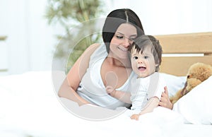 Beautiful young mother with a baby lying in bed and smiling