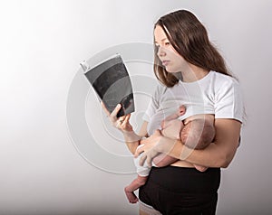 Beautiful young mother breastfeeding a baby while reading a black book